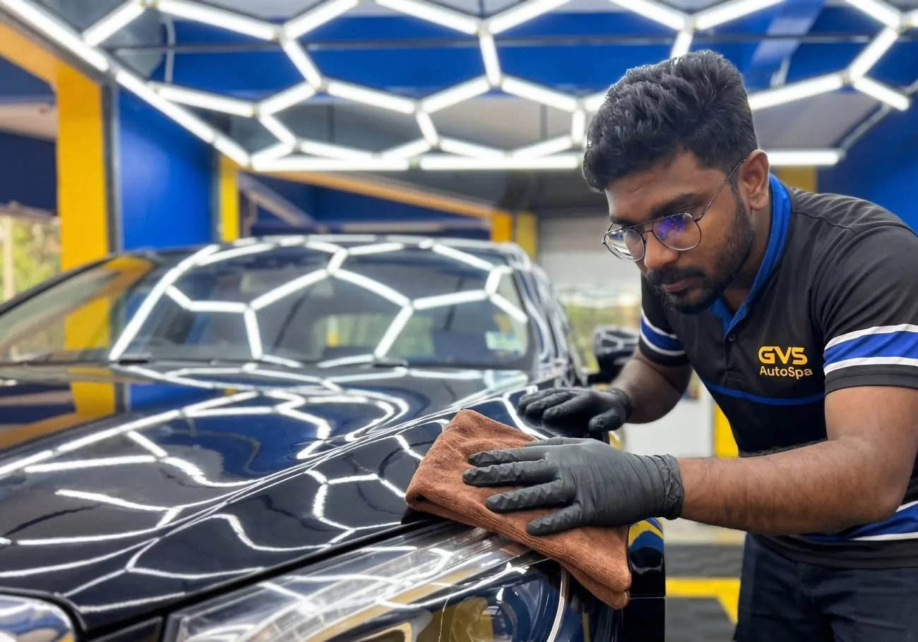 A technician hand-finishing a black car under the light rig